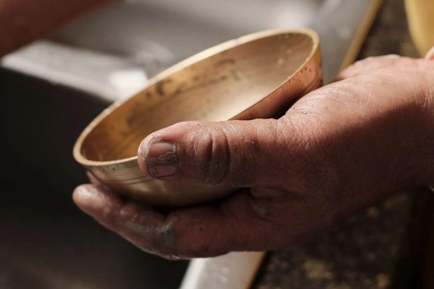 Weathered hands holding a brass bowl