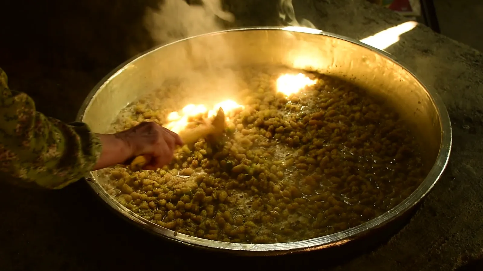 Herbs cooking slowly in a wide brass pan, steam rising